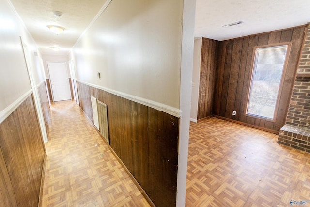 hall with ornamental molding, wooden walls, a textured ceiling, and light parquet floors