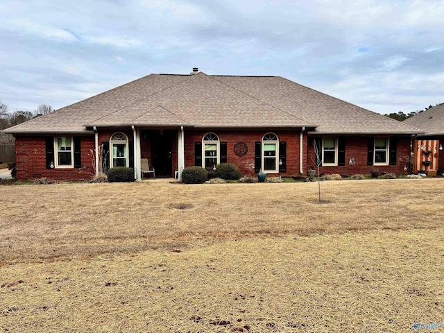 single story home with a shingled roof, a front yard, and brick siding