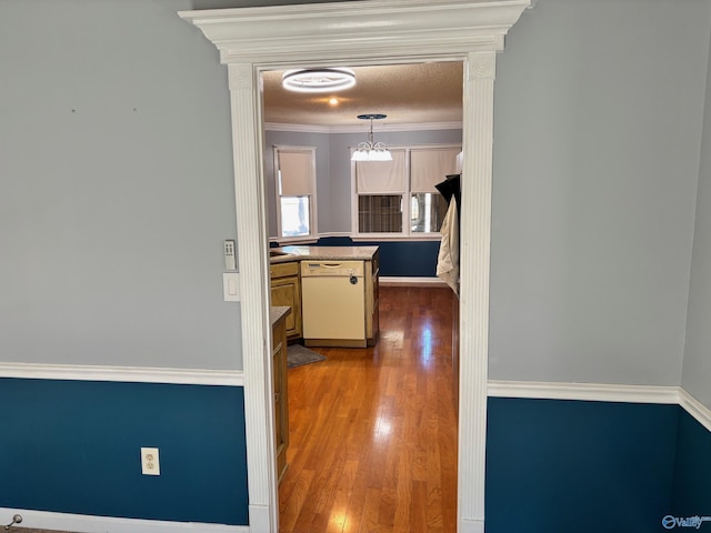 hall featuring a textured ceiling, ornamental molding, wood finished floors, and a chandelier