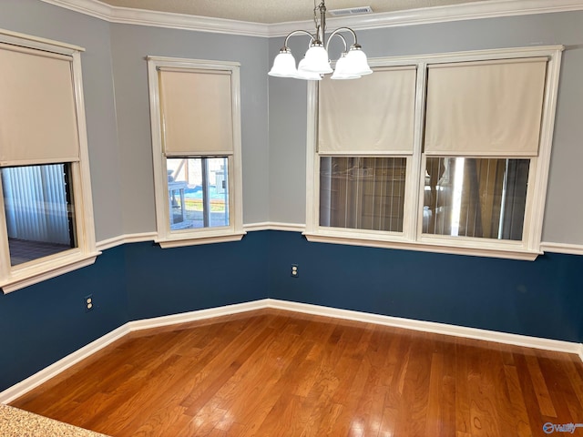 spare room featuring baseboards, visible vents, ornamental molding, wood finished floors, and a chandelier