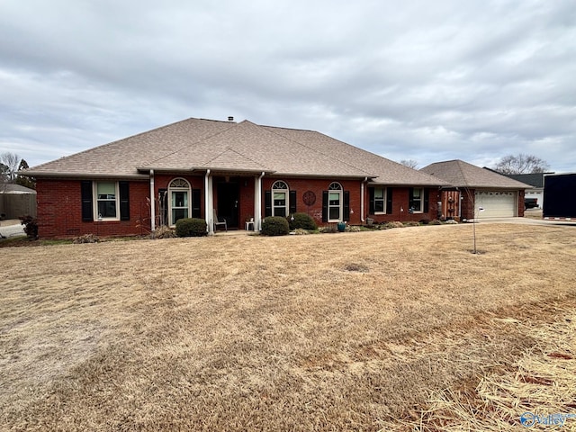 single story home with a shingled roof, a front yard, brick siding, and an attached garage