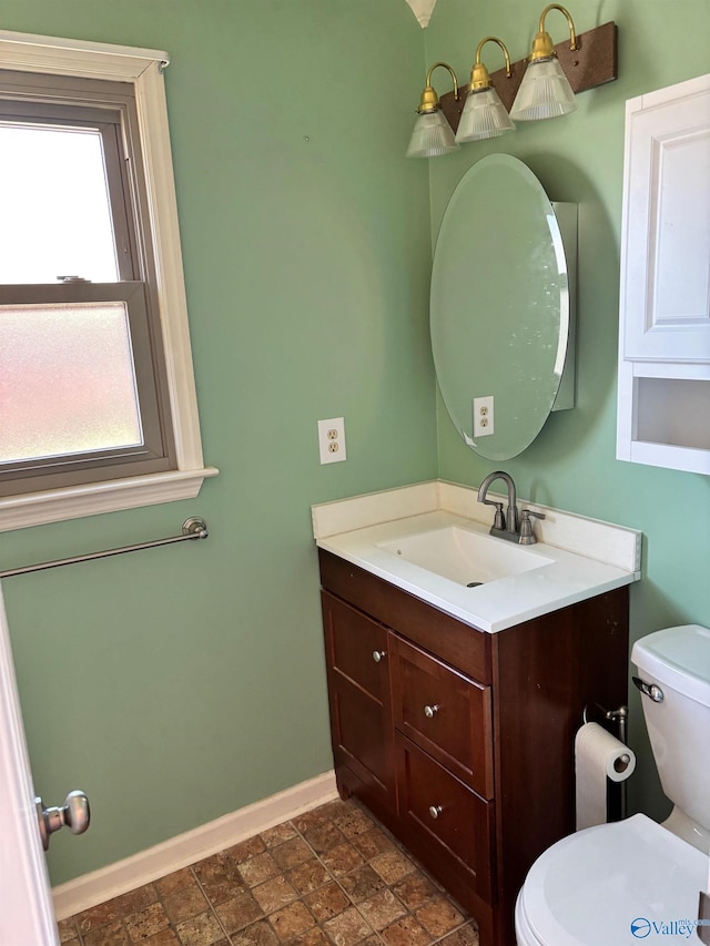 bathroom with toilet, stone finish flooring, baseboards, and vanity