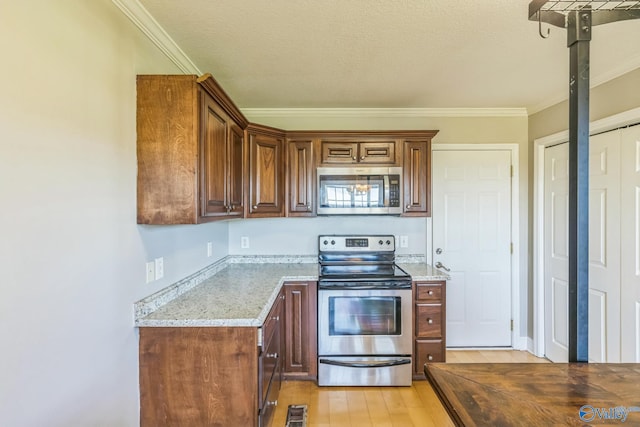 kitchen with ornamental molding, light stone counters, light hardwood / wood-style floors, and appliances with stainless steel finishes