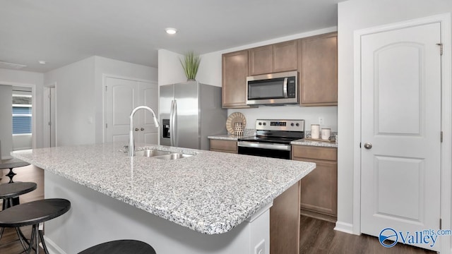 kitchen featuring a breakfast bar, sink, light stone counters, appliances with stainless steel finishes, and an island with sink