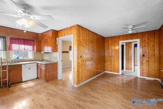 kitchen featuring wood walls, dishwasher, sink, ceiling fan, and light hardwood / wood-style flooring