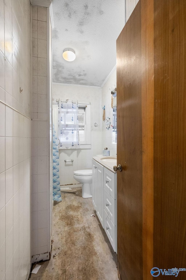 bathroom with tile walls, vanity, toilet, and a textured ceiling