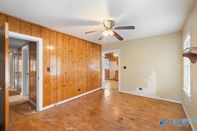 spare room with wood-type flooring, a wealth of natural light, ceiling fan, and wood walls