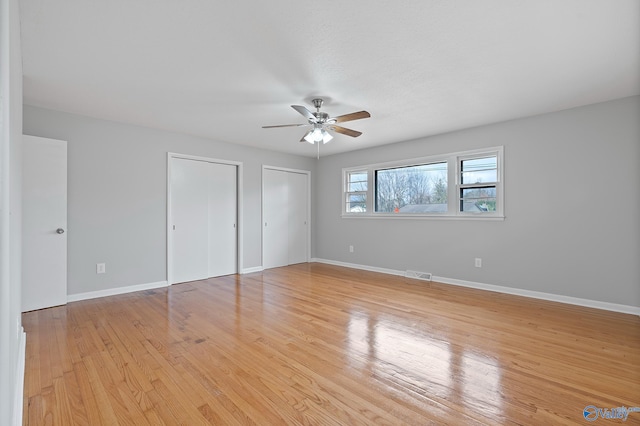 unfurnished bedroom with multiple closets, ceiling fan, and light hardwood / wood-style floors