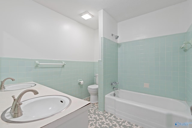 full bathroom with tiled shower / bath, tile walls, tile patterned flooring, vanity, and toilet