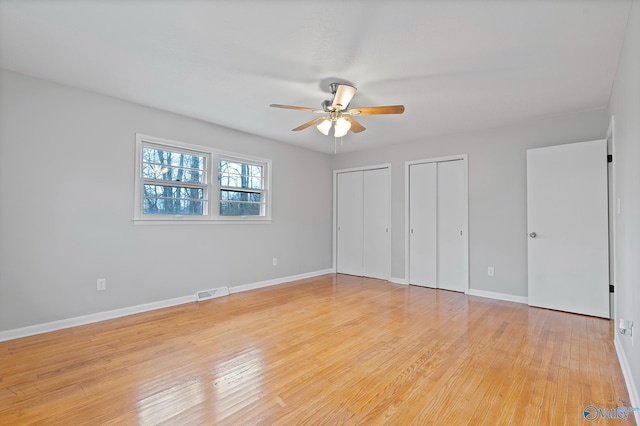 unfurnished bedroom with two closets, light hardwood / wood-style flooring, and ceiling fan