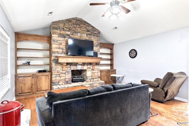 living room with ceiling fan, vaulted ceiling, a stone fireplace, and light hardwood / wood-style flooring