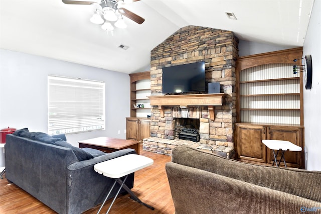 living room with wood-type flooring, vaulted ceiling, ceiling fan, and a stone fireplace