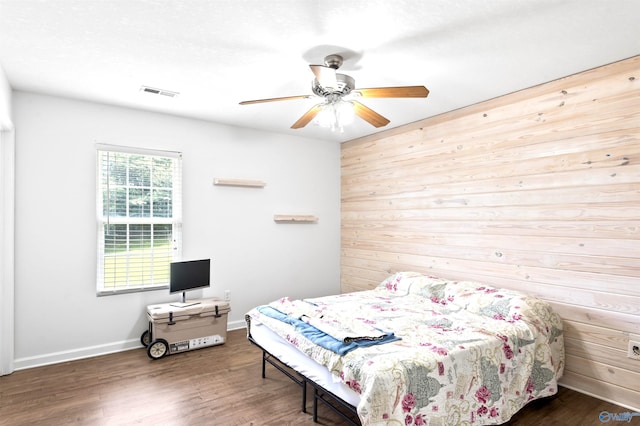 bedroom featuring ceiling fan, dark wood-type flooring, and wood walls