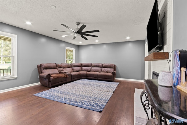 living room featuring a textured ceiling, a large fireplace, ceiling fan, and dark hardwood / wood-style flooring