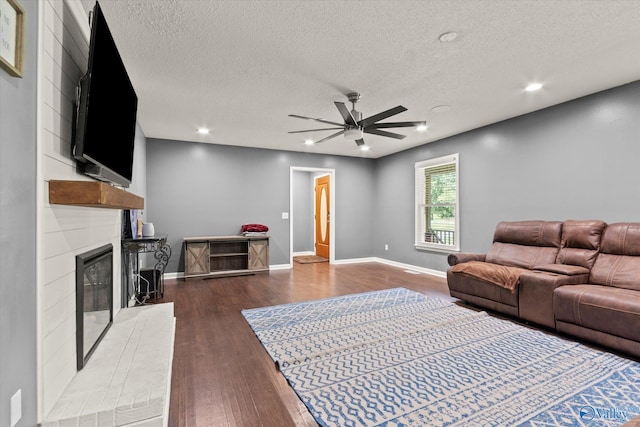 living room with a large fireplace, ceiling fan, hardwood / wood-style flooring, and a textured ceiling