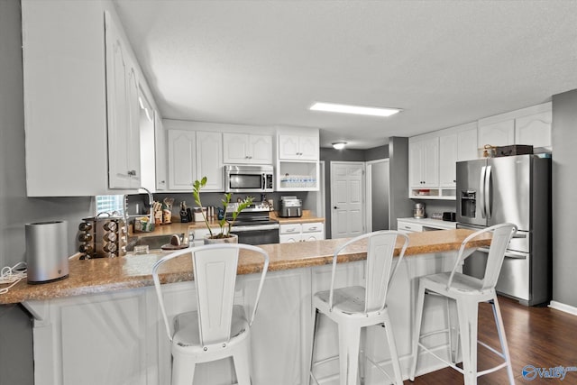 kitchen featuring a breakfast bar area, dark hardwood / wood-style floors, appliances with stainless steel finishes, kitchen peninsula, and white cabinets