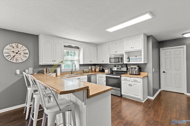 kitchen with stainless steel appliances, a kitchen breakfast bar, dark hardwood / wood-style flooring, kitchen peninsula, and sink