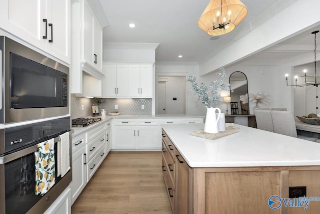 kitchen featuring light wood-type flooring, tasteful backsplash, white cabinetry, decorative light fixtures, and stainless steel appliances