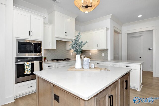 kitchen featuring appliances with stainless steel finishes, white cabinetry, a kitchen island, and light wood-type flooring