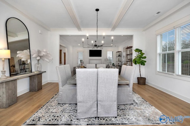 dining room with beamed ceiling, a notable chandelier, crown molding, and light wood-type flooring