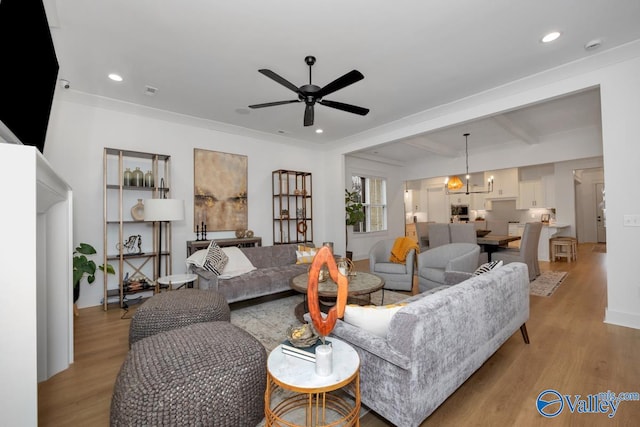 living room featuring light wood-type flooring, crown molding, beamed ceiling, and ceiling fan with notable chandelier