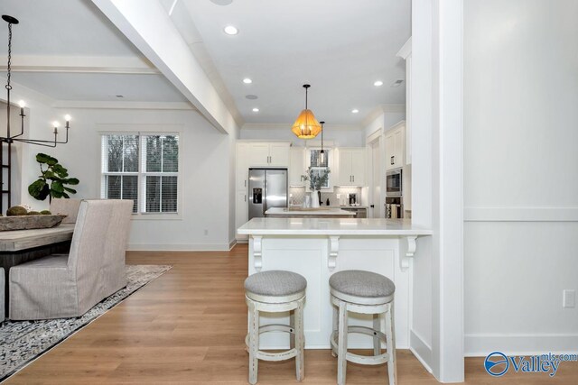 kitchen featuring light wood-type flooring, white cabinets, a breakfast bar, appliances with stainless steel finishes, and decorative light fixtures