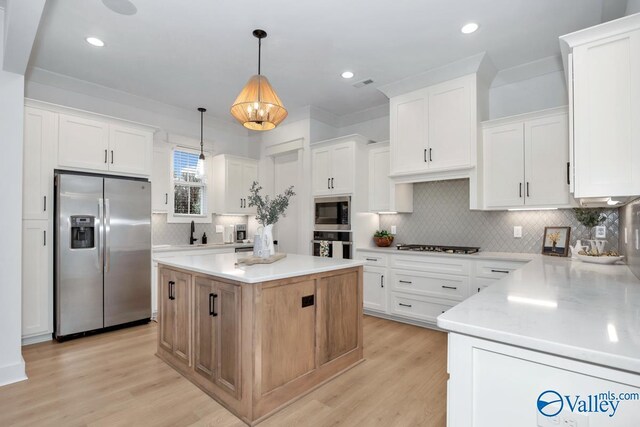 kitchen with appliances with stainless steel finishes, light hardwood / wood-style flooring, tasteful backsplash, white cabinets, and a kitchen island