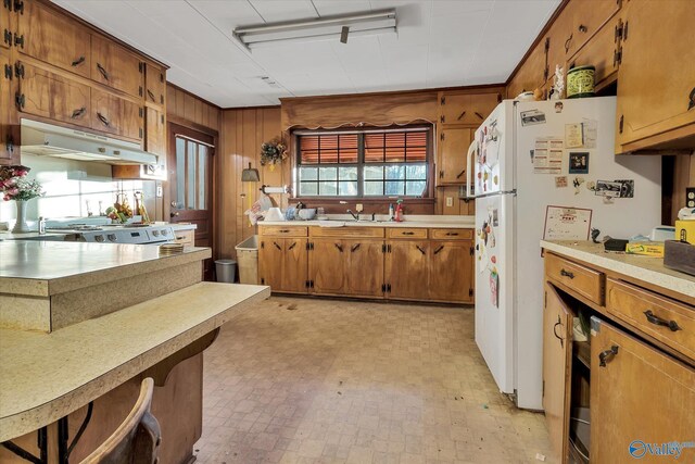 kitchen with white fridge, light tile patterned flooring, range, a kitchen bar, and wood walls