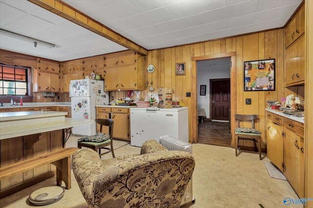 kitchen featuring white fridge, light hardwood / wood-style flooring, wooden walls, and sink