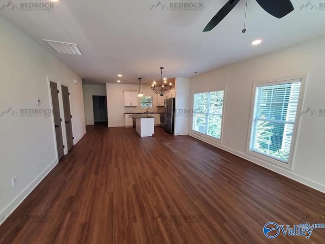 unfurnished living room featuring ceiling fan with notable chandelier and dark hardwood / wood-style flooring