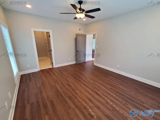 unfurnished bedroom with ensuite bath, ceiling fan, dark hardwood / wood-style floors, and multiple windows