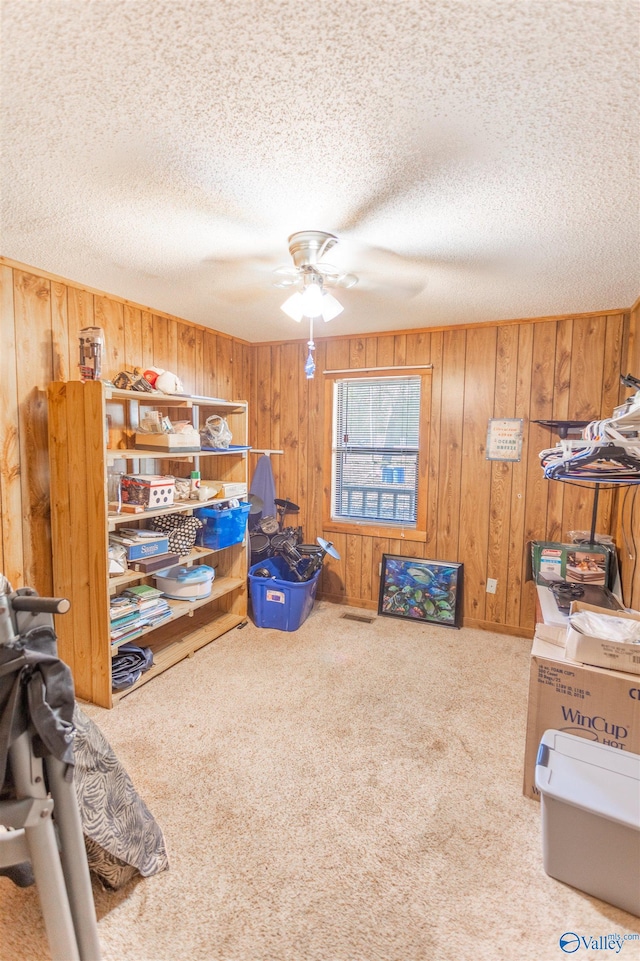 misc room featuring carpet floors, ceiling fan, a textured ceiling, and wooden walls