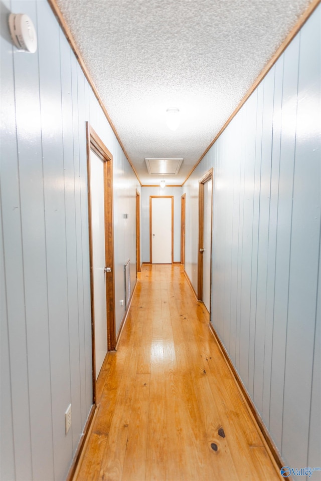 corridor with light hardwood / wood-style floors, crown molding, and a textured ceiling