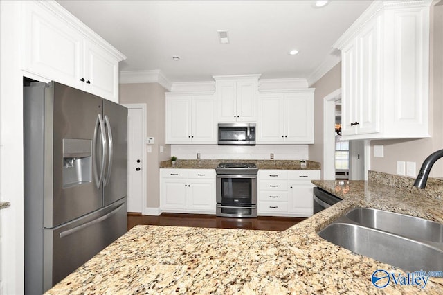 kitchen with light stone countertops, appliances with stainless steel finishes, crown molding, sink, and white cabinetry