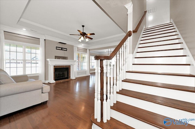 living room featuring ornamental molding, dark wood-type flooring, a healthy amount of sunlight, and a brick fireplace