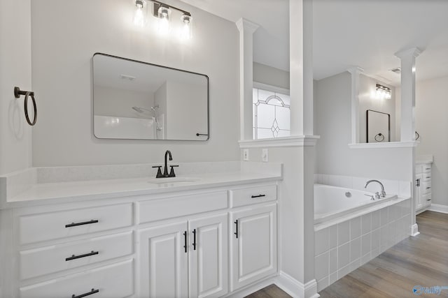 full bathroom featuring a garden tub, wood finished floors, baseboards, vanity, and ornate columns