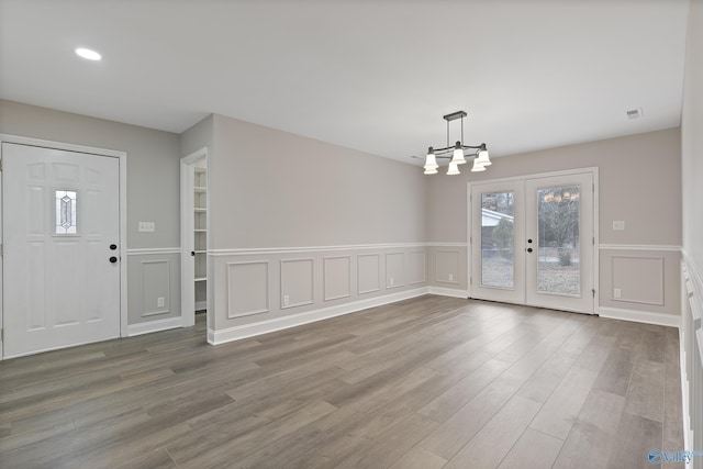 unfurnished dining area with a chandelier, visible vents, wood finished floors, and a decorative wall