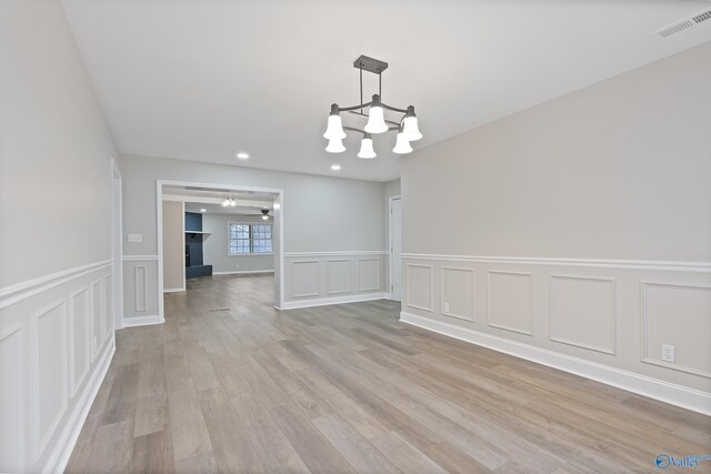 unfurnished dining area with visible vents, a fireplace, light wood-style floors, a decorative wall, and ceiling fan with notable chandelier