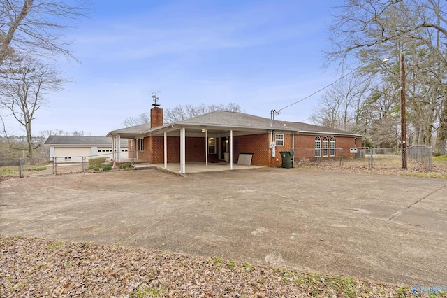 back of property with a gate, fence, concrete driveway, brick siding, and a chimney