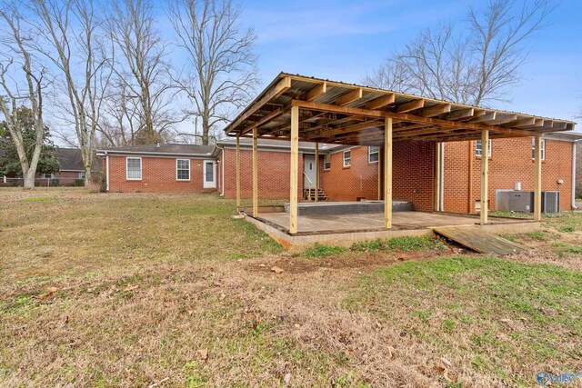 back of property featuring brick siding, a lawn, cooling unit, a carport, and a patio