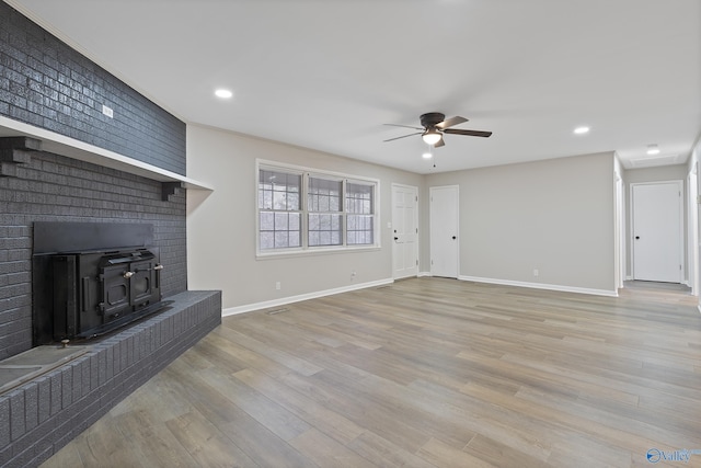 unfurnished living room featuring a ceiling fan, wood finished floors, baseboards, a wood stove, and recessed lighting