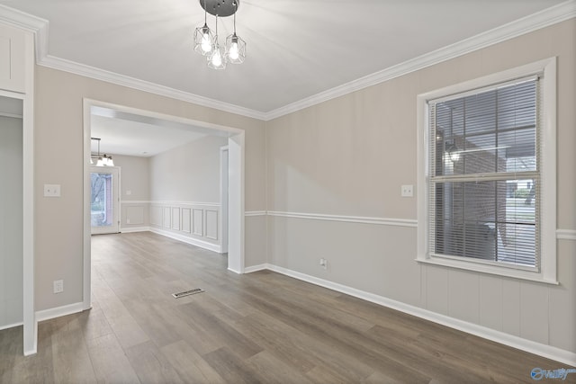 empty room with visible vents, a chandelier, ornamental molding, wood finished floors, and a decorative wall