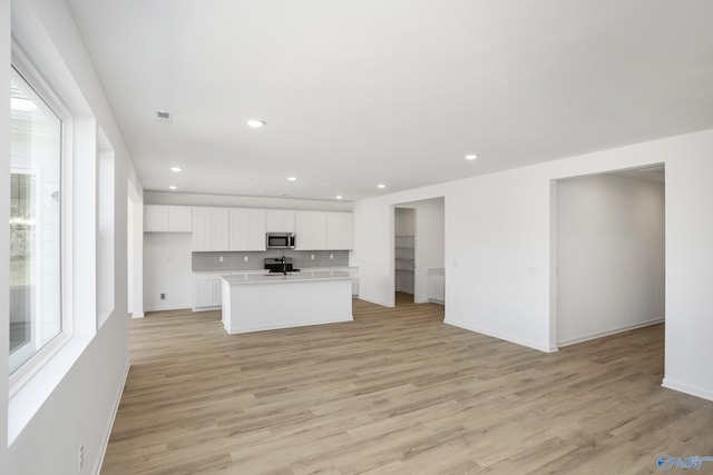 kitchen with white cabinetry, stainless steel appliances, backsplash, an island with sink, and light hardwood / wood-style floors