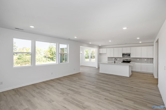 kitchen featuring appliances with stainless steel finishes, tasteful backsplash, a kitchen island with sink, light hardwood / wood-style floors, and white cabinetry