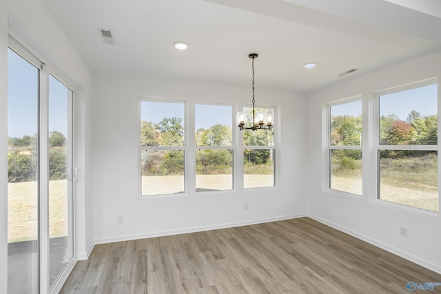 unfurnished dining area with hardwood / wood-style floors, plenty of natural light, and a chandelier