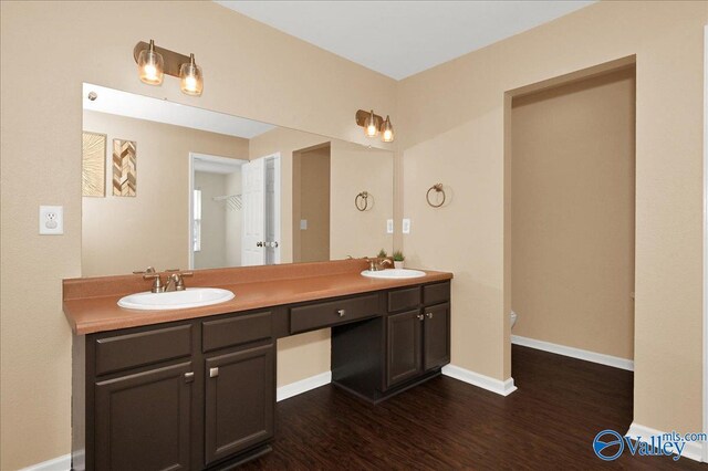 bathroom with double vanity, wood finished floors, a sink, and baseboards