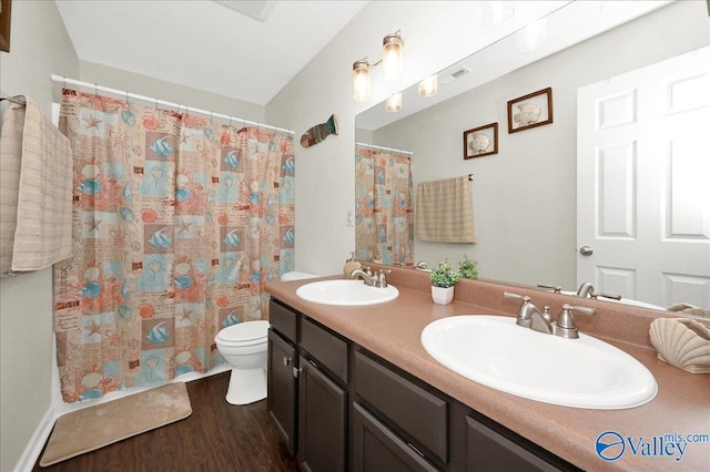 full bath with toilet, double vanity, a sink, and wood finished floors