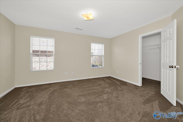 unfurnished bedroom with dark carpet, a walk in closet, and baseboards