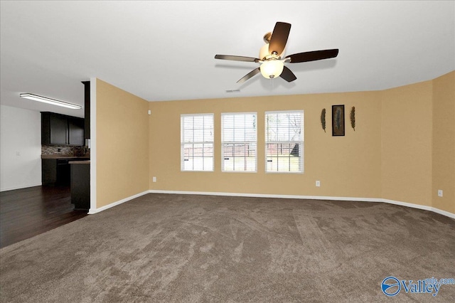 unfurnished living room featuring visible vents, dark colored carpet, a ceiling fan, and baseboards