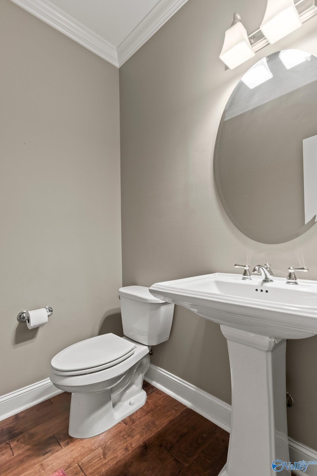 half bathroom with wood finished floors, toilet, ornamental molding, a sink, and baseboards